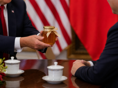 A suited diplomat presents a jar of honey during a formal U.S.-China meeting