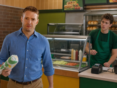 Jason Tate walking out of a sandwich shop with a wrapped footlong while an employee watches from behind the counter