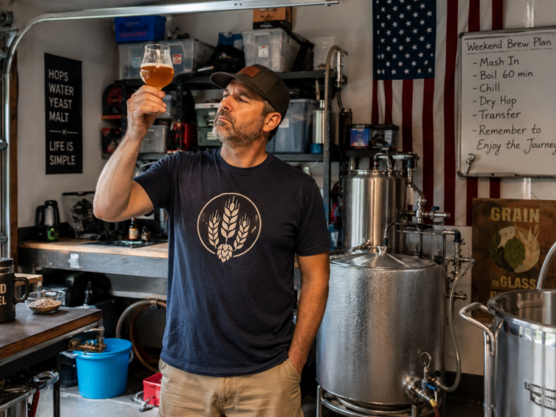 A father inspecting a glass of beer in a home garage brewing setup.