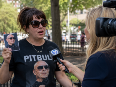 A woman wearing a Pitbull shirt holding a photo of the musician during a news interview.