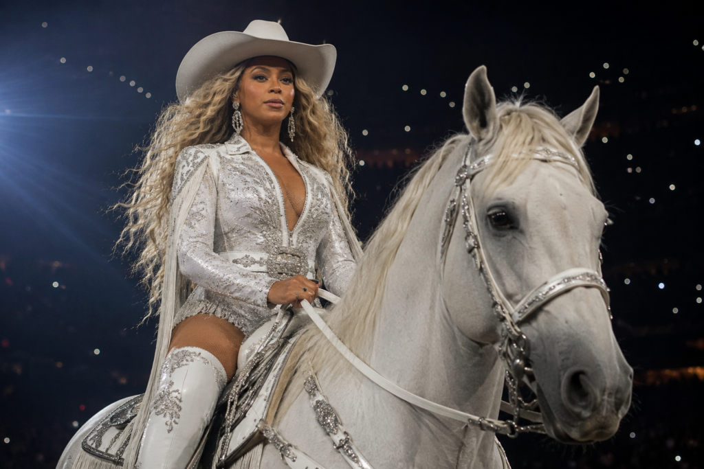 Beyonce in a white cowboy outfit riding onstage during a stadium performance