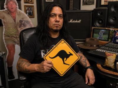 Fear Factory guitarist Dino Cazares holding a kangaroo crossing sign in a studio surrounded by Australian souvenirs