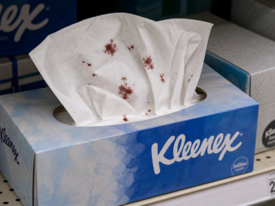 A Kleenex tissue box on a store shelf with tissues pulled out and marked by dark red bloodlike stains.