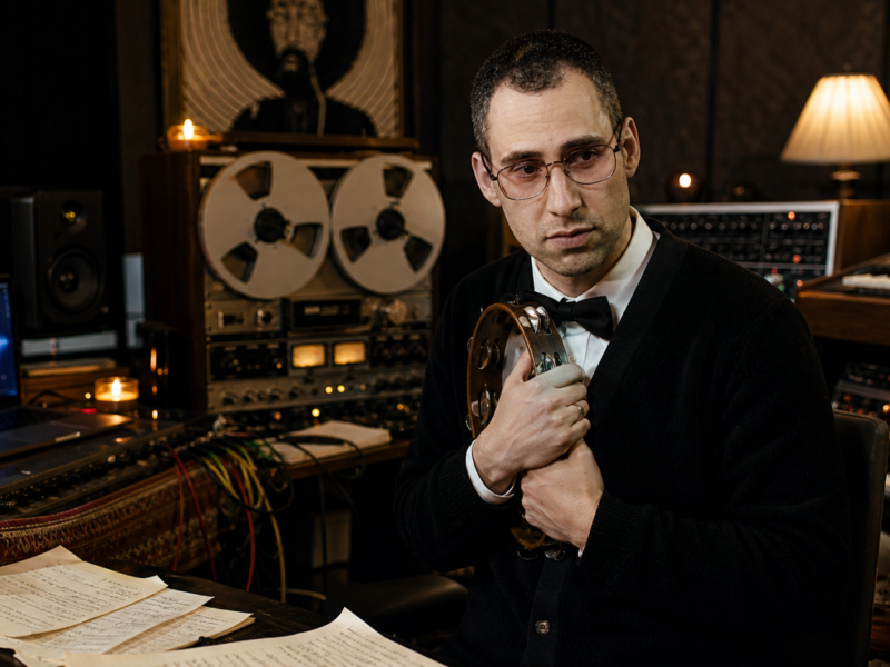 Jack Antonoff-inspired pop producer in a staged recording studio guarding an analog tape machine like a sacred object.