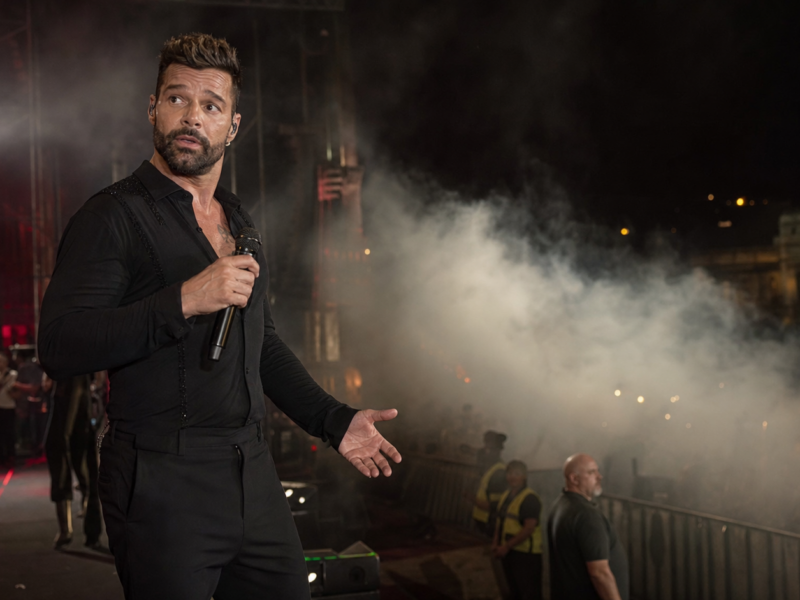 Ricky Martin performing on a night concert stage as pale haze drifts beside the crowd barrier.