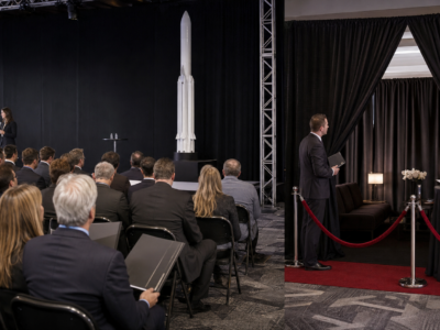 Investors watch a rocket-company IPO presentation beside a discreet VIP lounge.