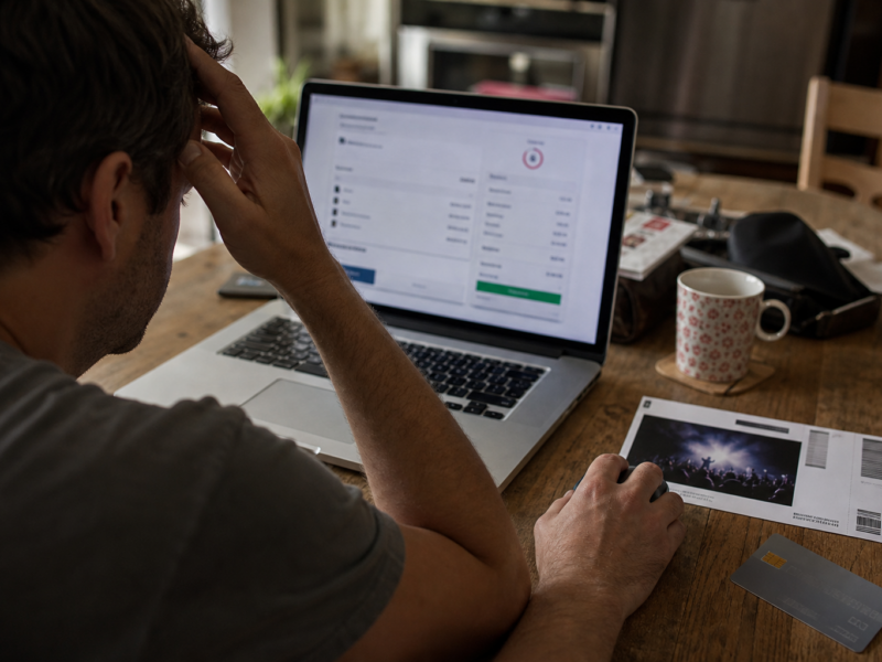Laptop checkout page on kitchen table with ticket printout and credit card