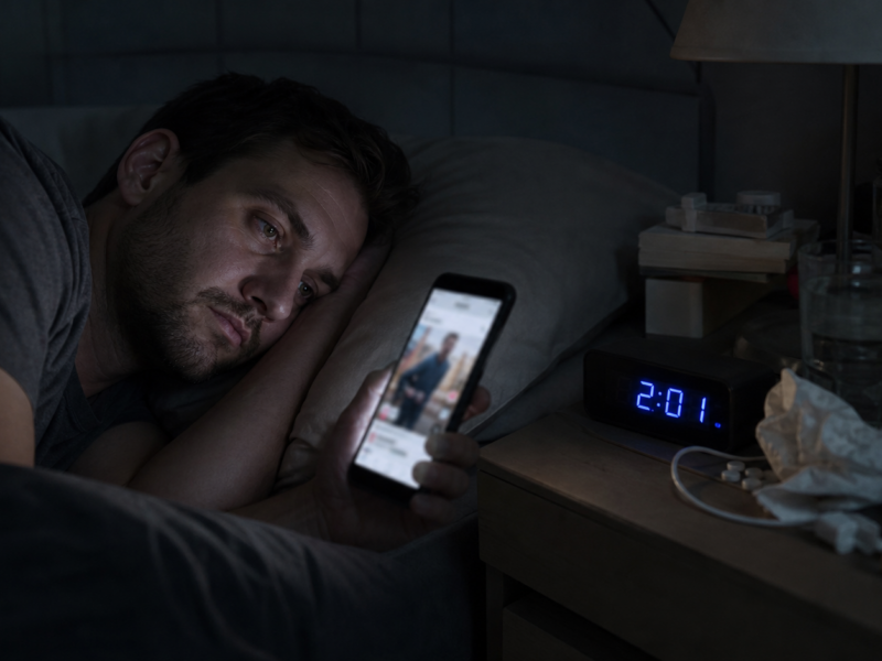 Awake adult staring at a phone in a dark bedroom